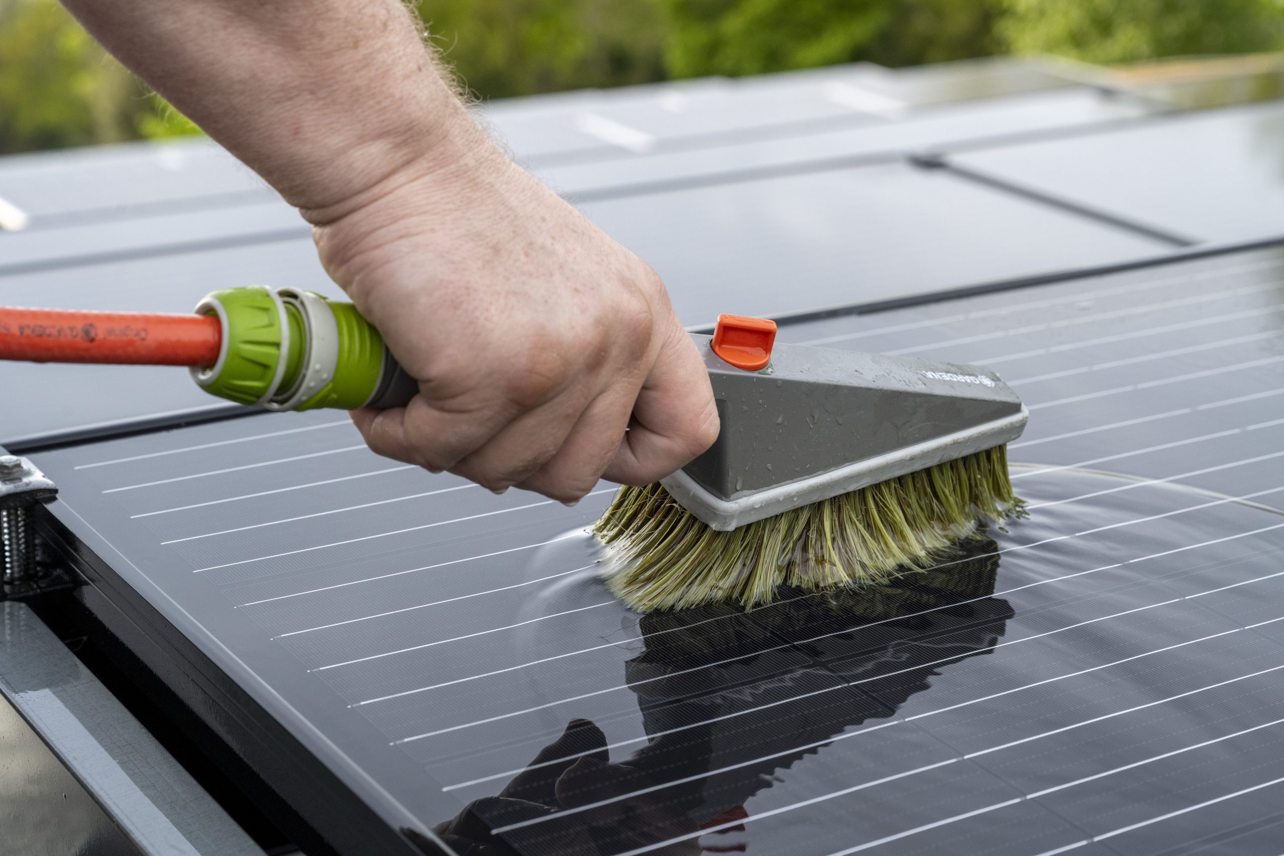 Close-up of a hand holding a brush cleaning the surface of a solar panel.